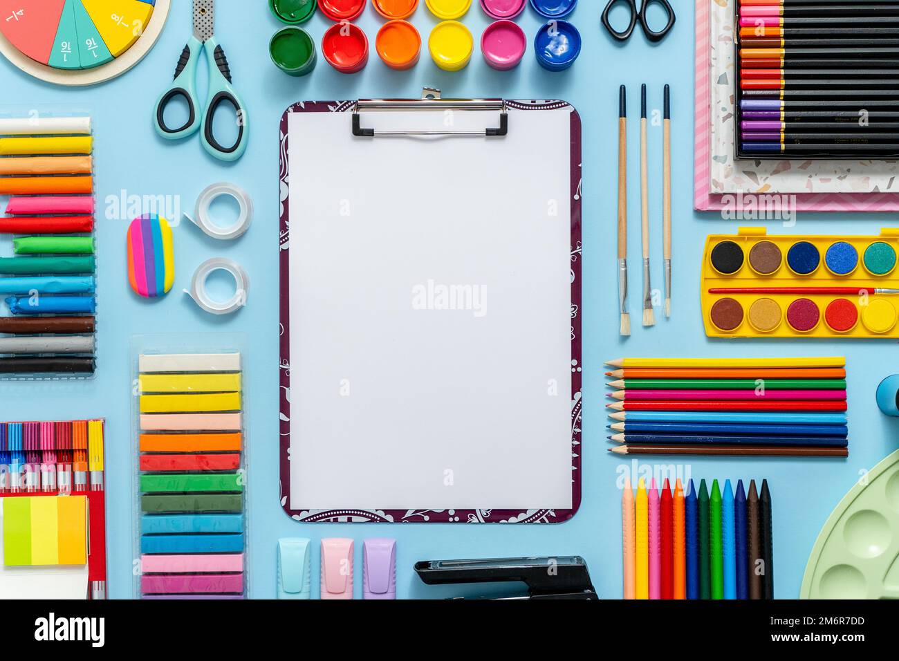 Colorful school supplies placed on blue background with white plain paper in the middle Stock Photo