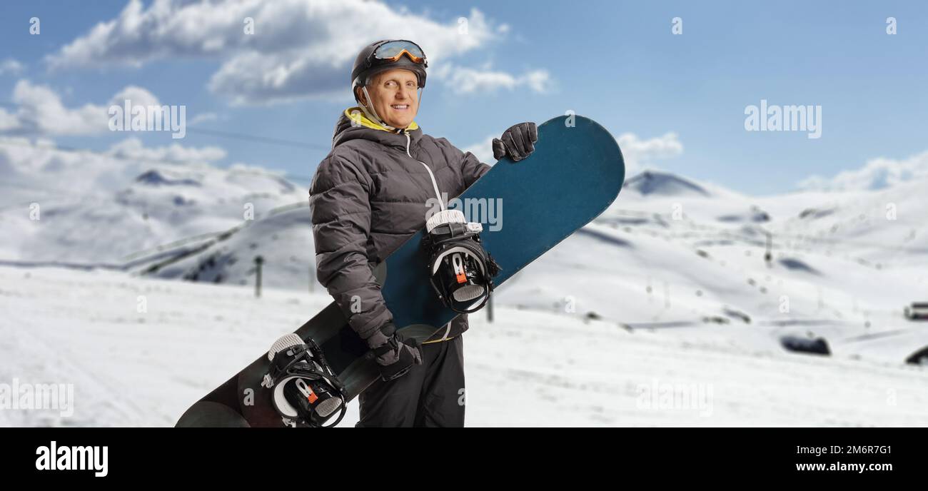 Mature man with a snowboard standing on a mountain and looking at camera Stock Photo