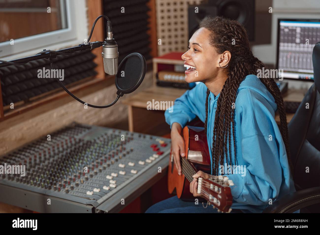 Enthusiastic African young woman musician plays guitar and records song ...