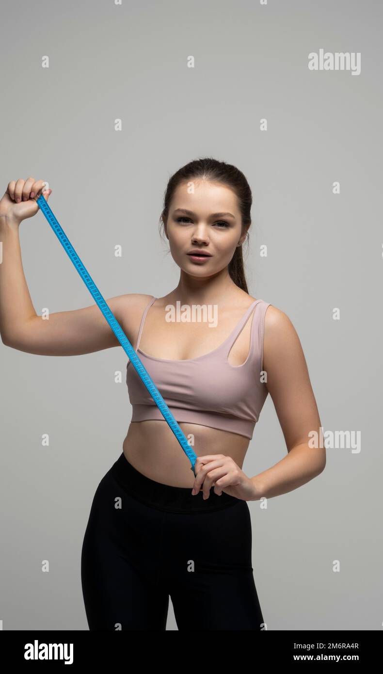 Happy slim brunette woman in sport wear with measuring tape on white ...