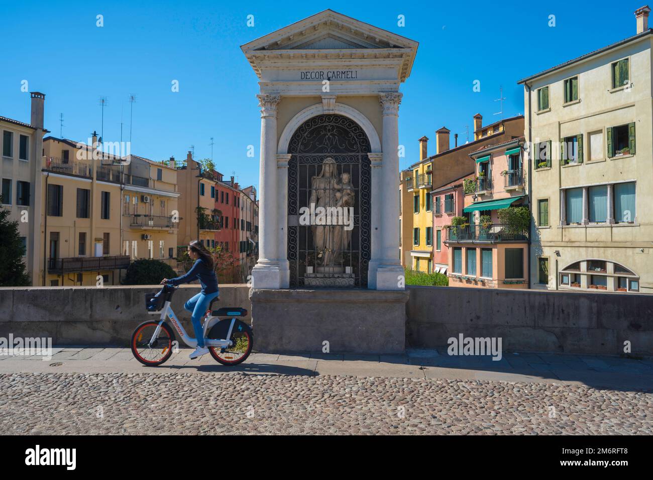 Madonna shrine Italy, view of a young woman cycling past a Madonna And Child sited in a niche on the Ponte Molino (Roman Bridge) in Padua, Italy Stock Photo