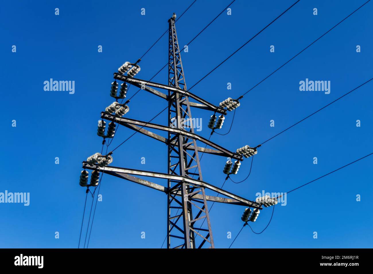 High voltage power pylons against blue sky and sun rays Stock Photo - Alamy
