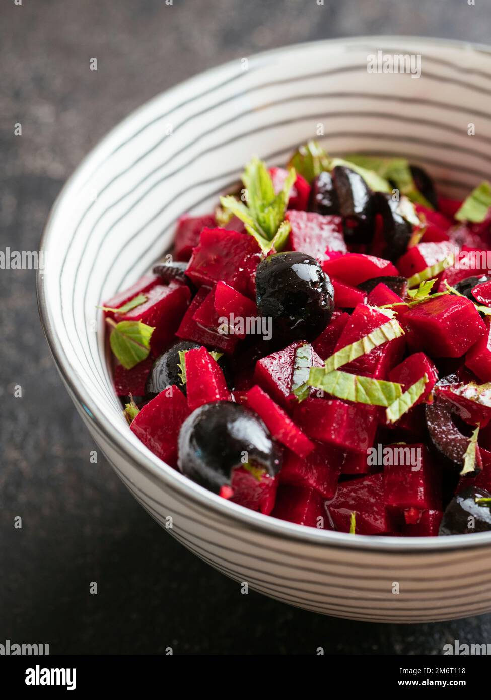 Bowl with a home made beet salad with minted beets, olives and fresh mint leaves. Stock Photo