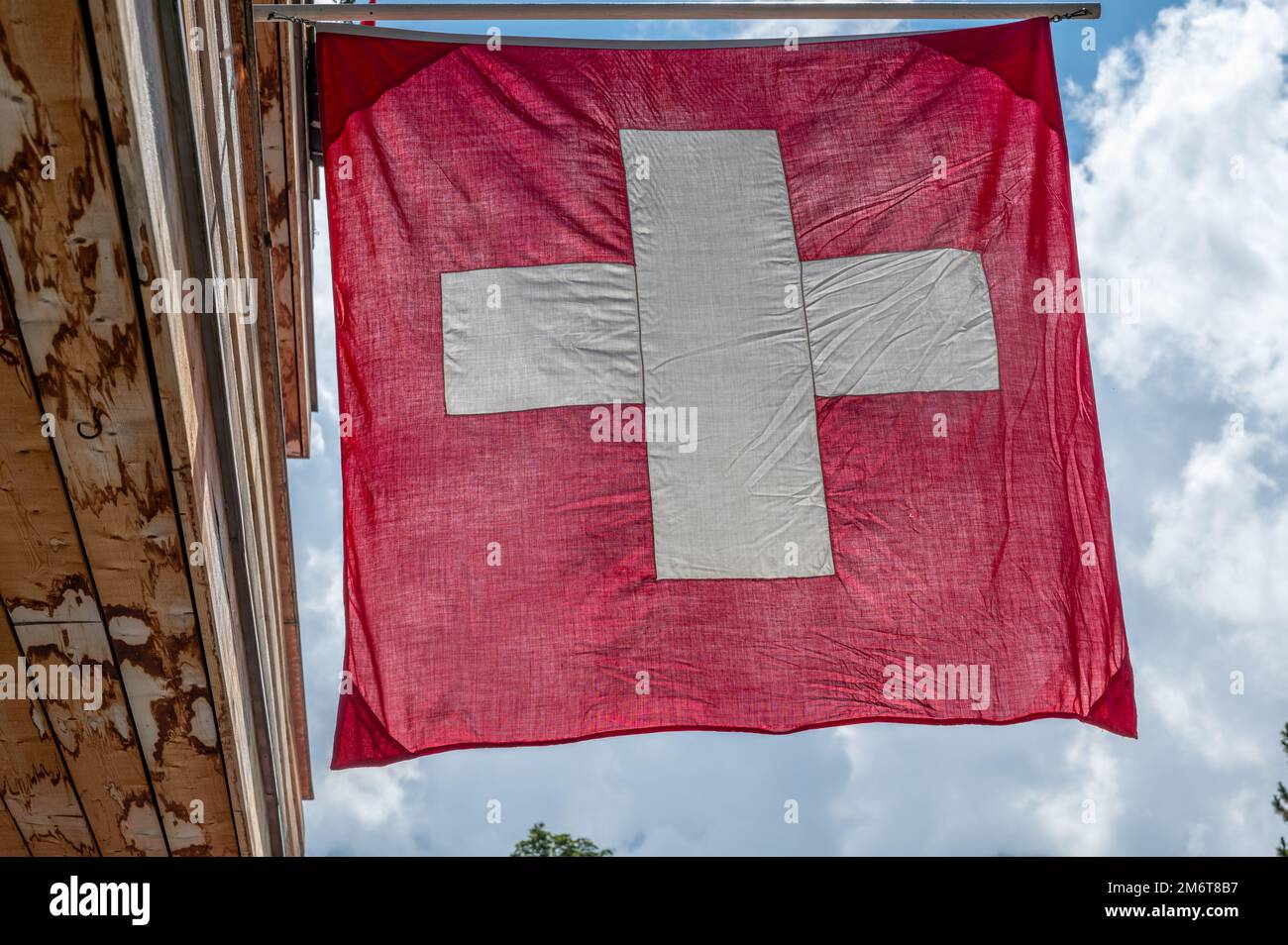 Swiss flag. Switzerland flag hanging on roof against blue sky. One red square flag with a white cross in the centre. Objects. Stock Photo