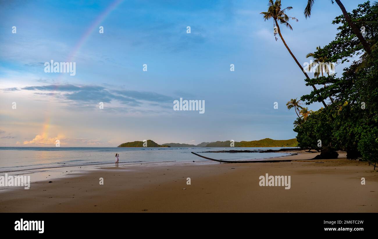 Asian women looking at a rainbow on the beach after a monsoon rain storm in Thailand Stock Photo