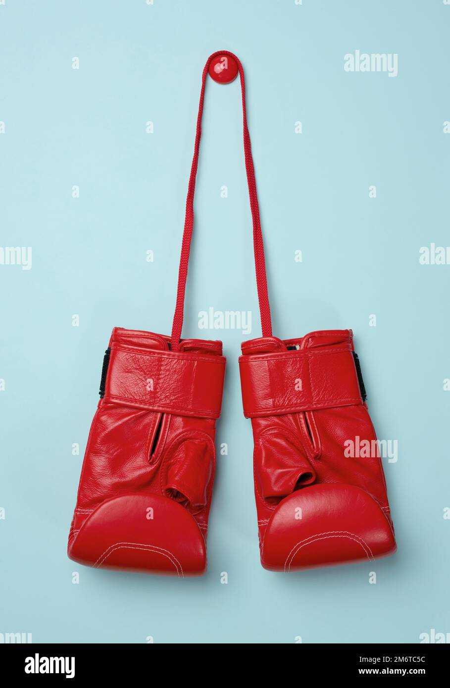 Red leather boxing gloves hanging on a cord, blue background. Stock Photo