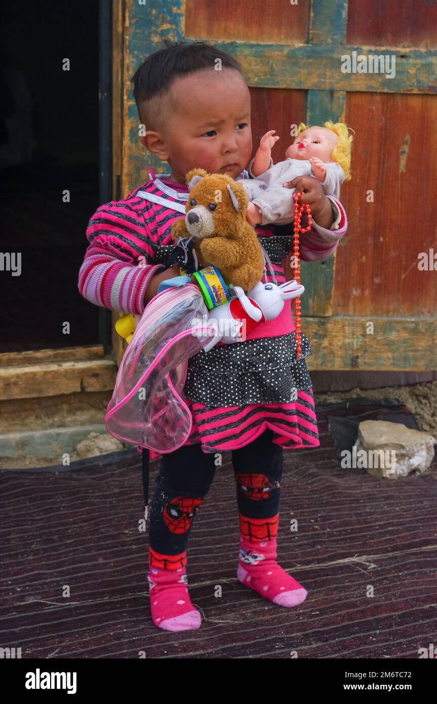 Near Ak Baital, Gorno-Badakshan, Tajikistan - 07 31 2013 : Portrait of cute Kyrgyz toddler girl outside yurt holding her doll, teddy bear and rabbit Stock Photo