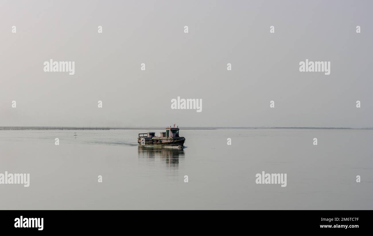 Minimalist landscape view of small wooden ferry boat crossing the mighty Brahmaputra river in Assam, India Stock Photo