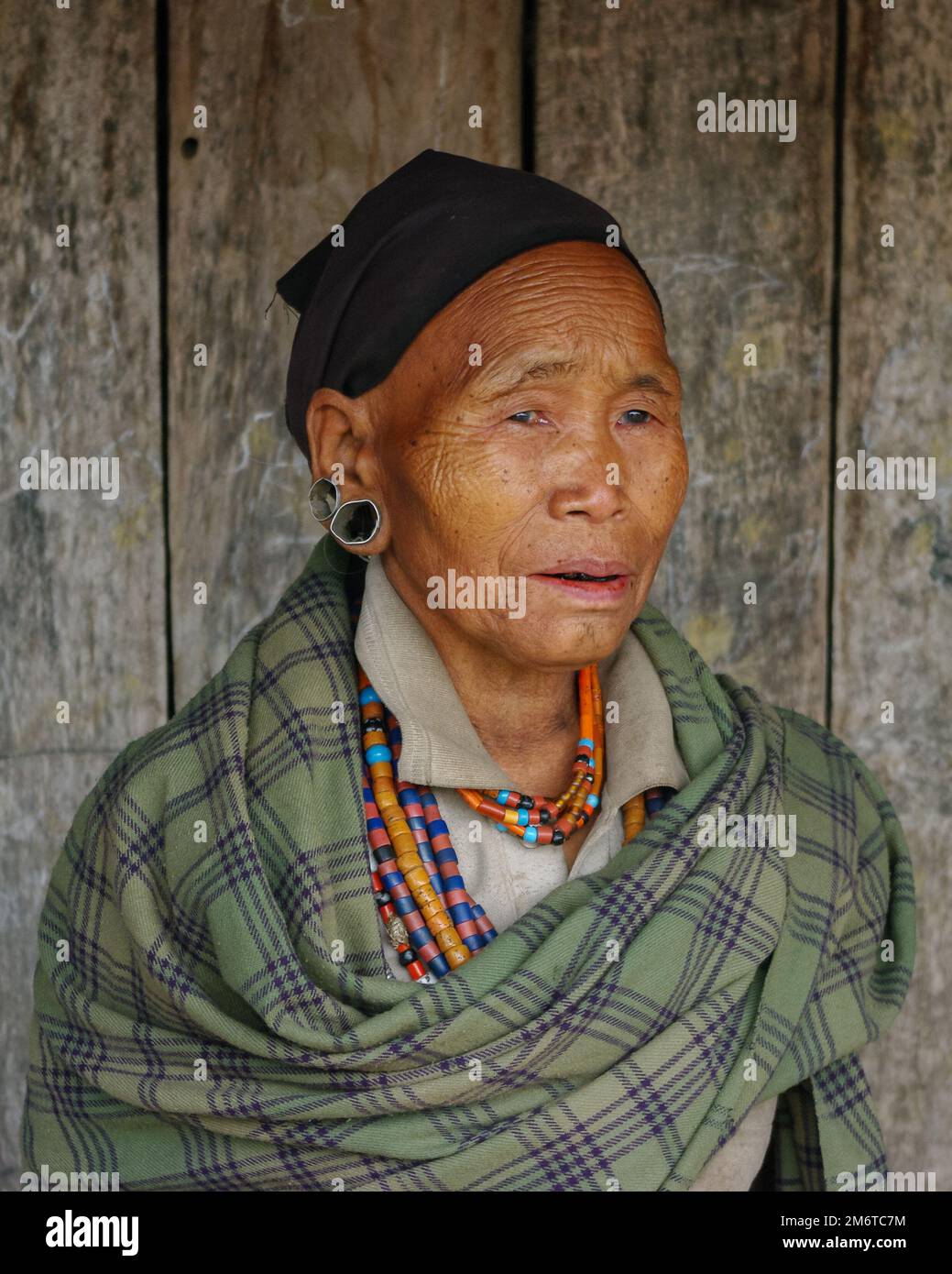 Mon, Nagaland, India - 03 03 2009 : Portrait of old ethnic Naga woman wearing green plaid, traditional necklace and black scarf on wooden background Stock Photo