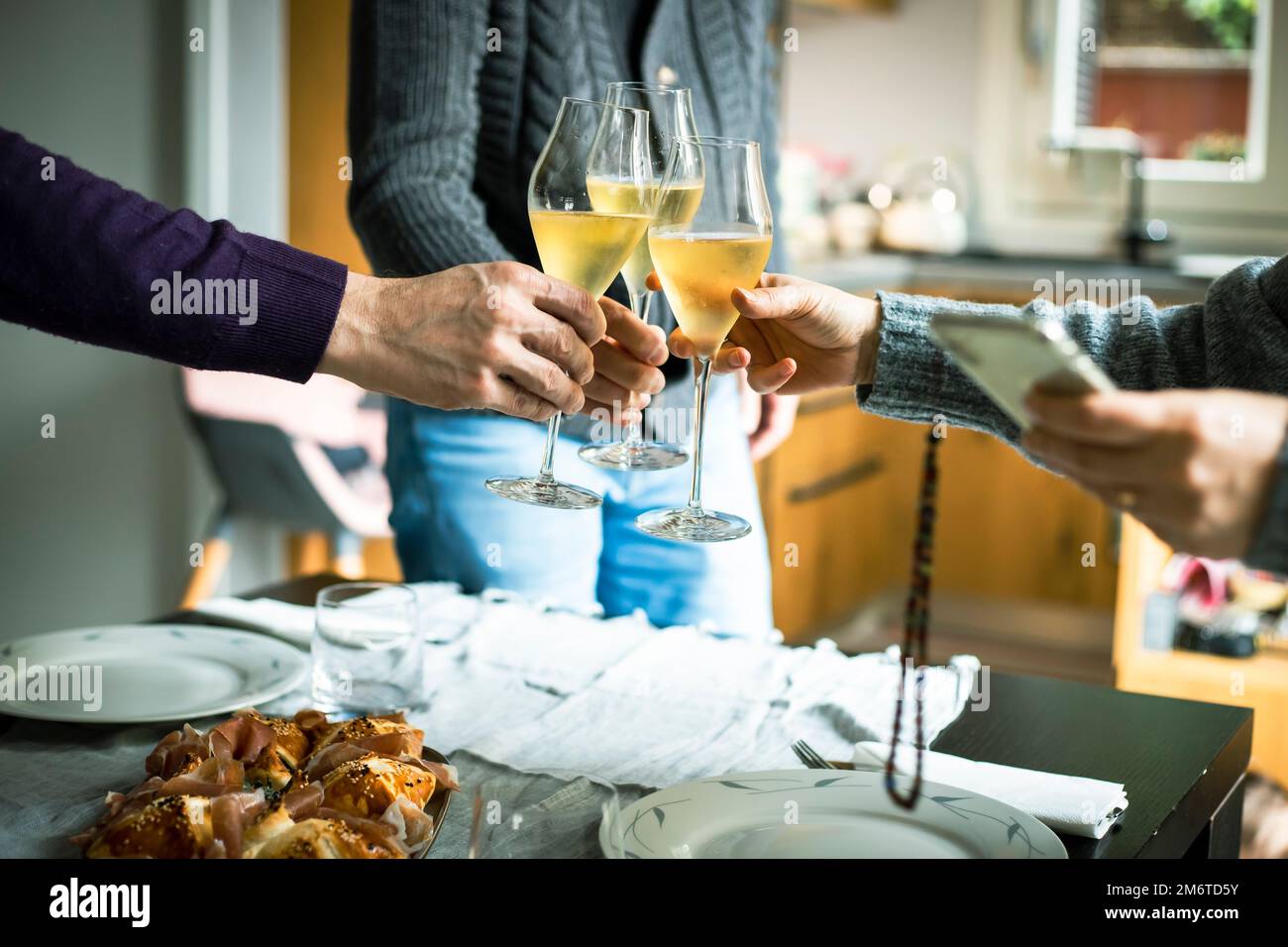 Three people celebrate Christmas by clinking glasses of prosecco at their home celebration dinner. Stock Photo