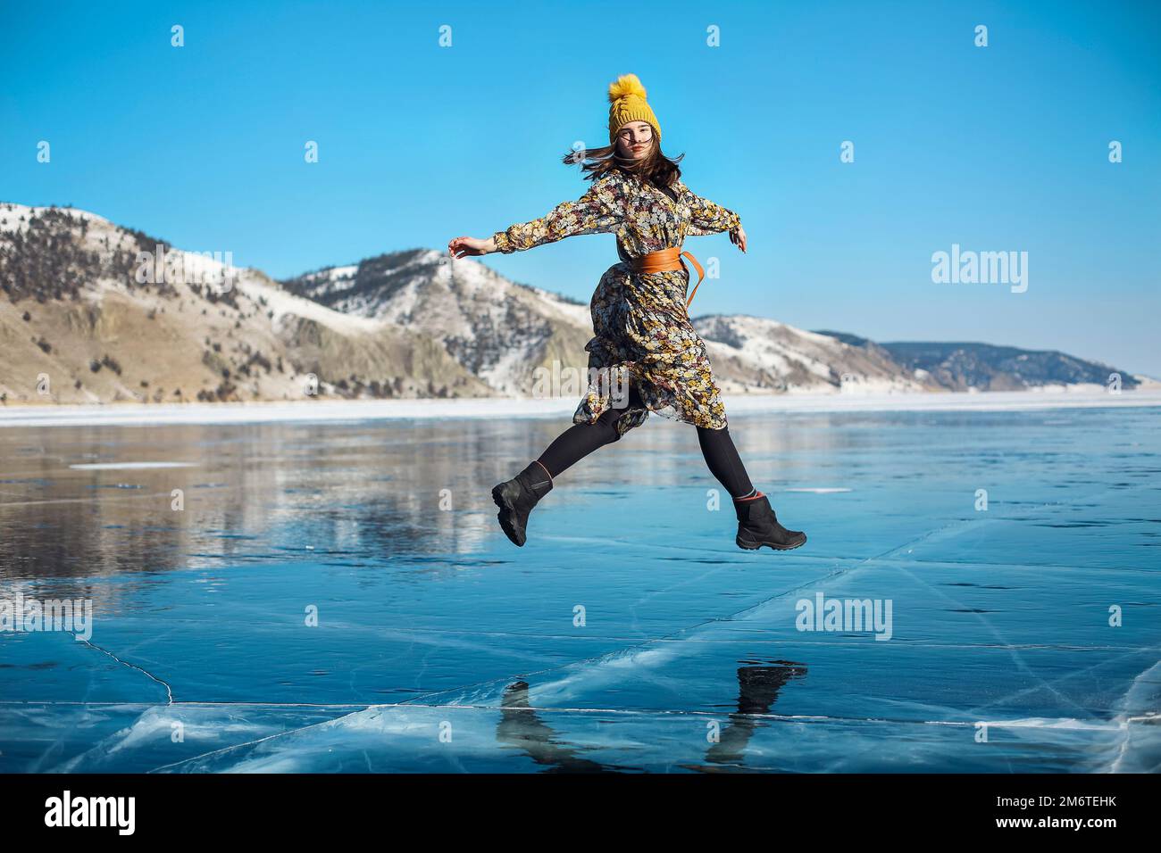 Fashionable image of a stunning woman posing on Baikal Lake ice wearing yellow hat Stock Photo