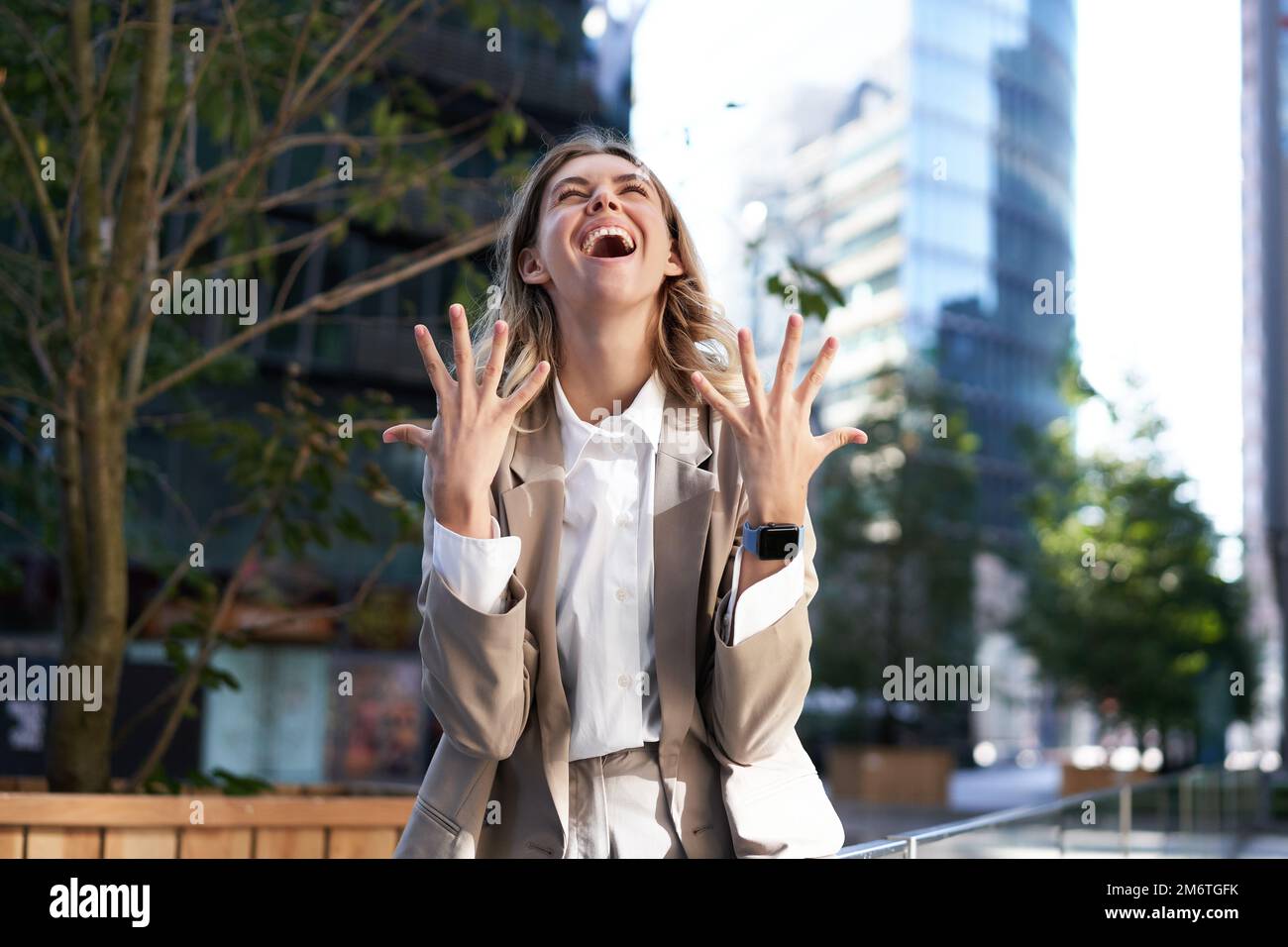 Enthusiastic businesswoman rejoicing, celebrating and feeling happy, express pure joy, standing on street in beige suit Stock Photo