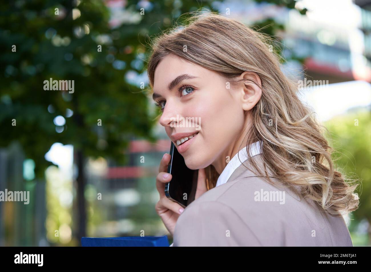 Close up portrait of corporate woman calling on mobile phone, walking on street with work documents in hand, wearing business su Stock Photo