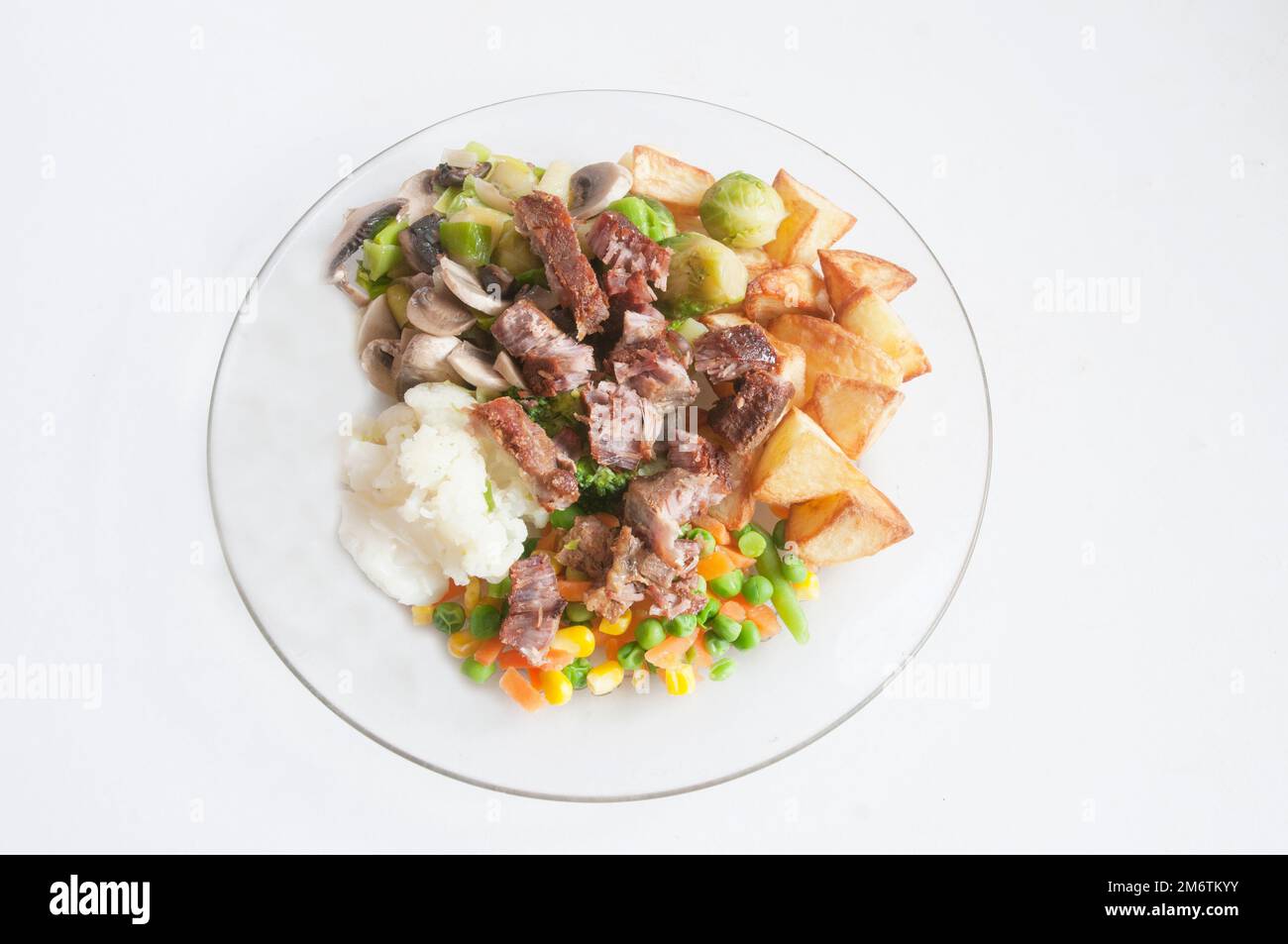 Cooked meal on a glass dinner plate a meat and vegetable meal of Pork & Crackling Cauliflower Brussel Sprouts Broccoli Mushrooms and Roast Potatoes Stock Photo