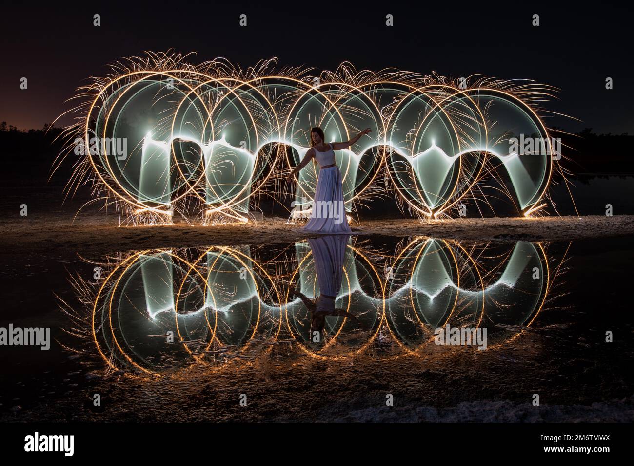 Woman posing for light painting with bright lights in the dark. Reflection in the water Stock Photo