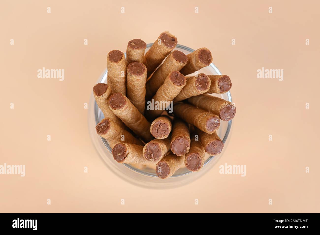 Jar of tasty wafer rolls with boiled condensed milk on beige background ...