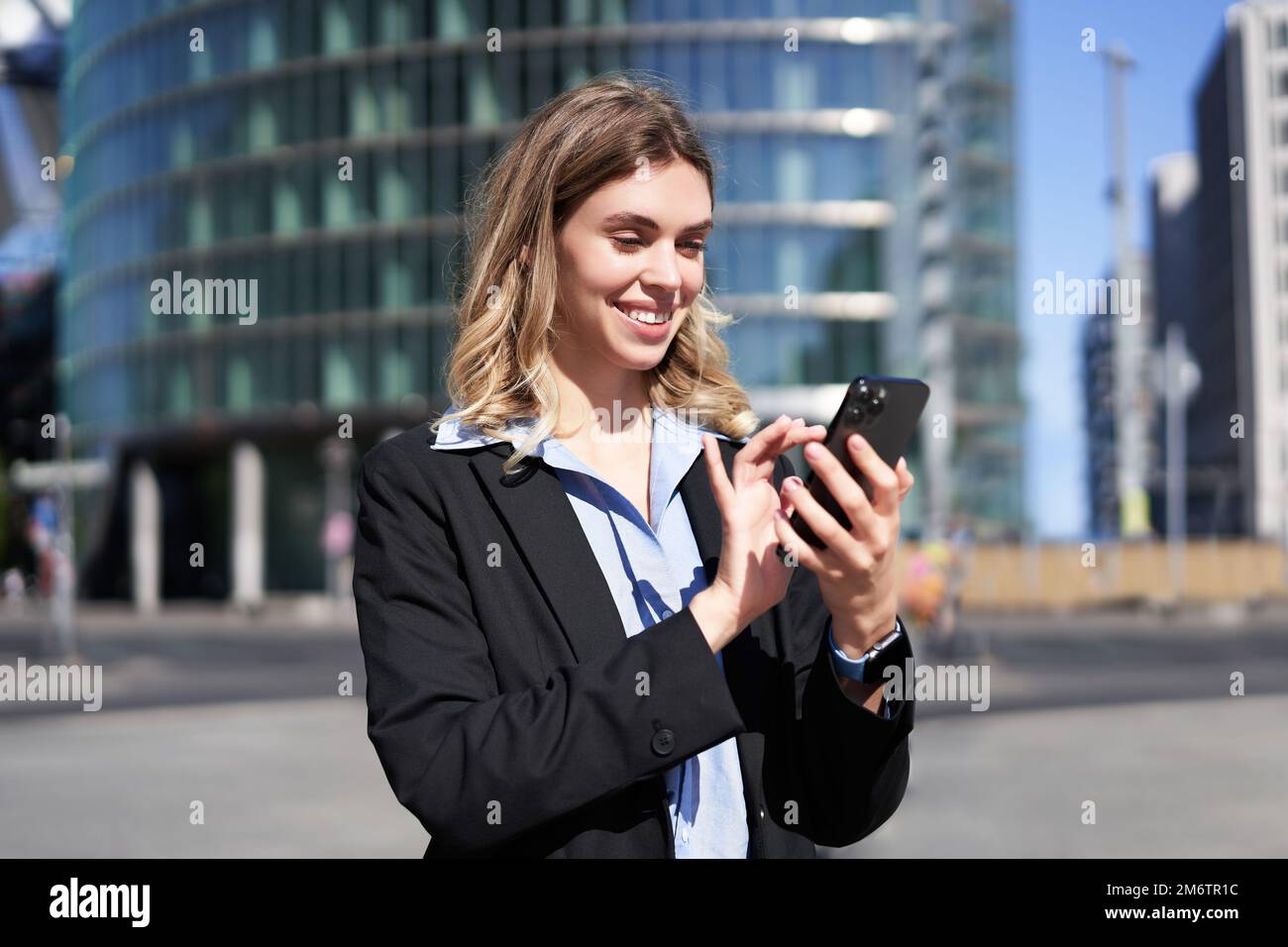 Portrait of confident corporate woman using mobile phone on city street. Businesswoman messaging on smartphone app while standin Stock Photo