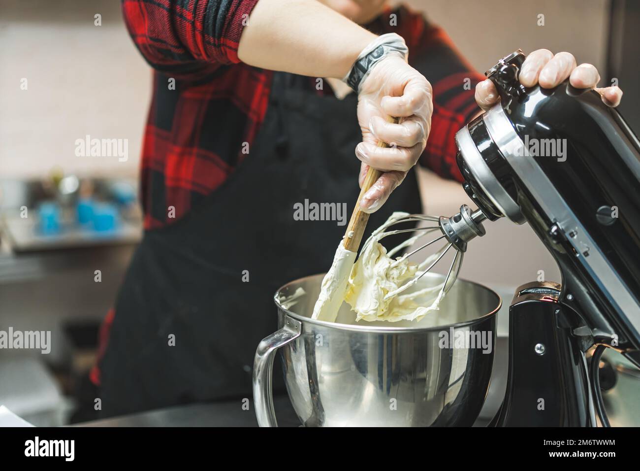 Bakery equipment. Caucasian person using spatula and standing mixer to create fluffy buttercream frosting. High quality photo Stock Photo