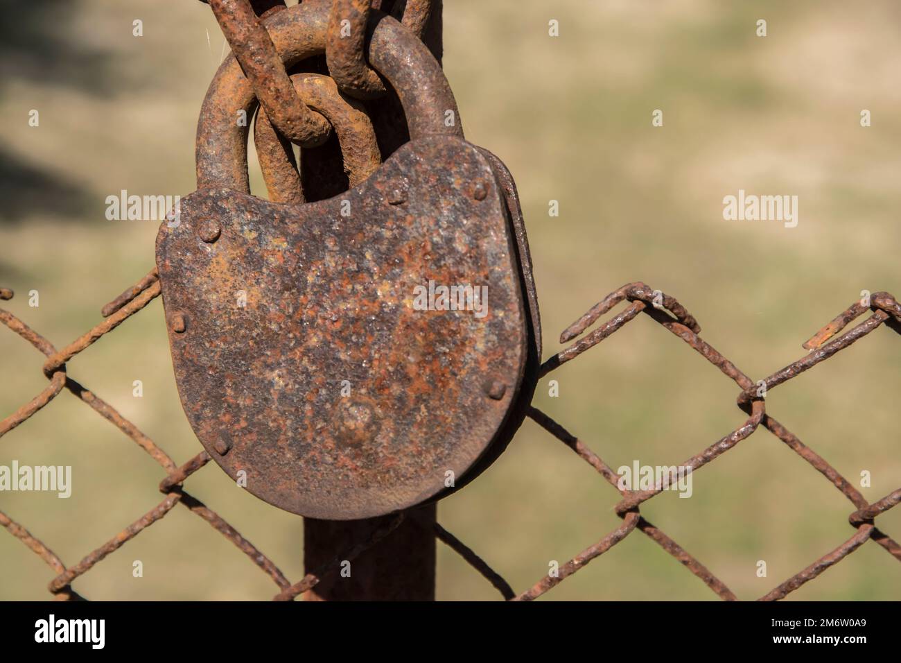 Old weathered rusty padlock locked on iron fence grid closeup Stock Photo