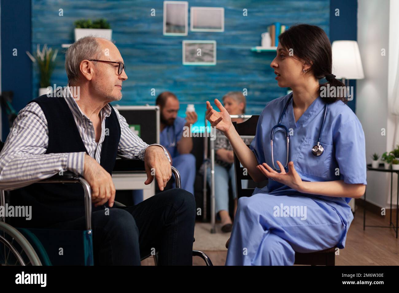 Female health specialist explaining rehabilitation therapy to an elderly patient in a wheelchair