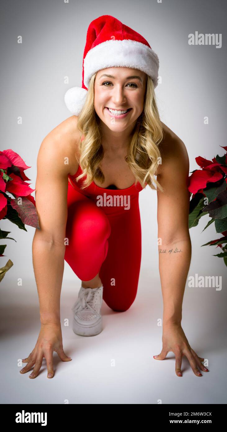 Smiling Young Woman in Sprinters Stance | Poinsettia plant | christmas holiday | christmas hat Stock Photo