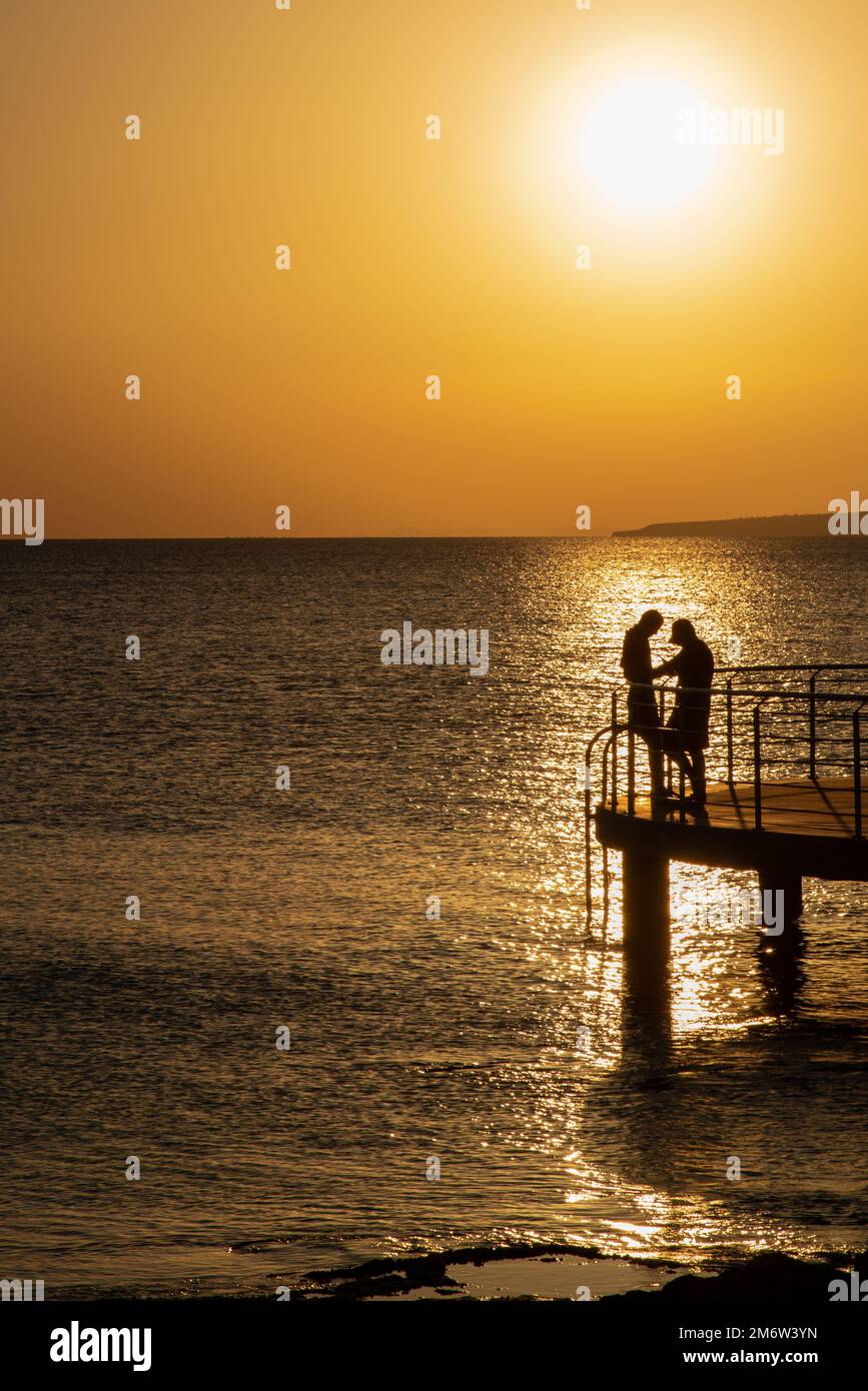 Silhouette of young couple enjoying beautiful sunset at beach. Romantic moment human relationship Stock Photo