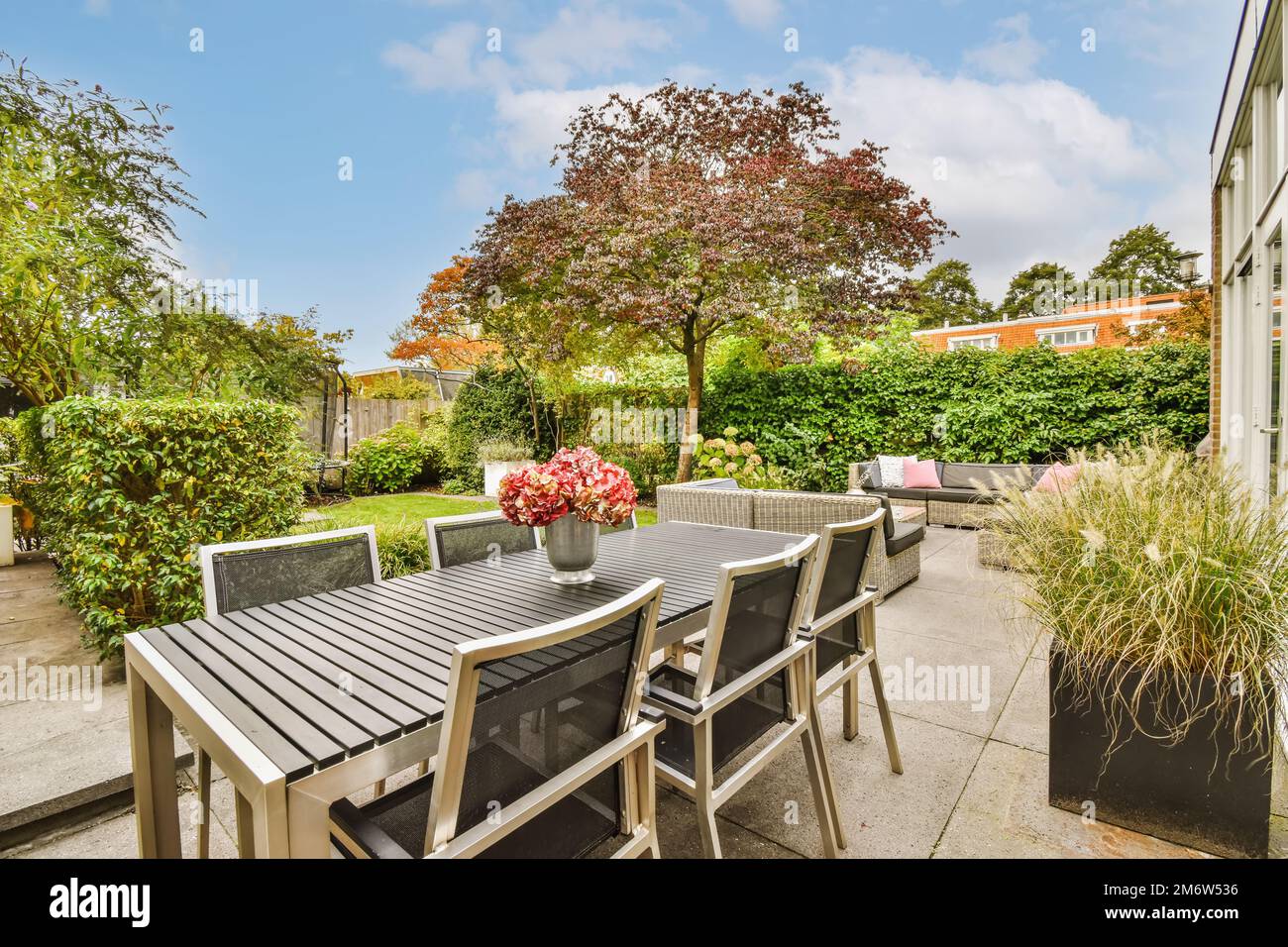 a table and chairs on a patio with trees in the back ground, bushes and ...