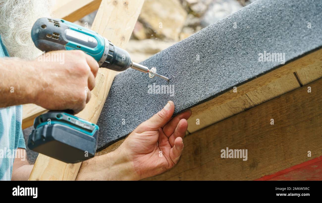 Men's hands in work gloves with a yellow screwdriver screw the roofing  sheet to the roof of a country house. Cordless drill Stock Photo - Alamy