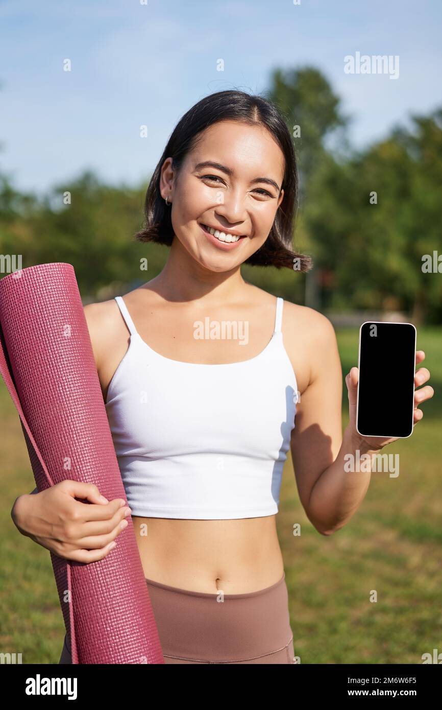 Vertical shot of fit and healthy young asian woman, shows smartphone screen with her workout stats, recommends telephone applica Stock Photo