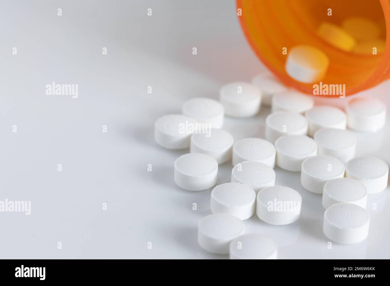 round, white tablet pills spilt out of a medicine bottle on a white background with copy space, shallow depth of field Stock Photo