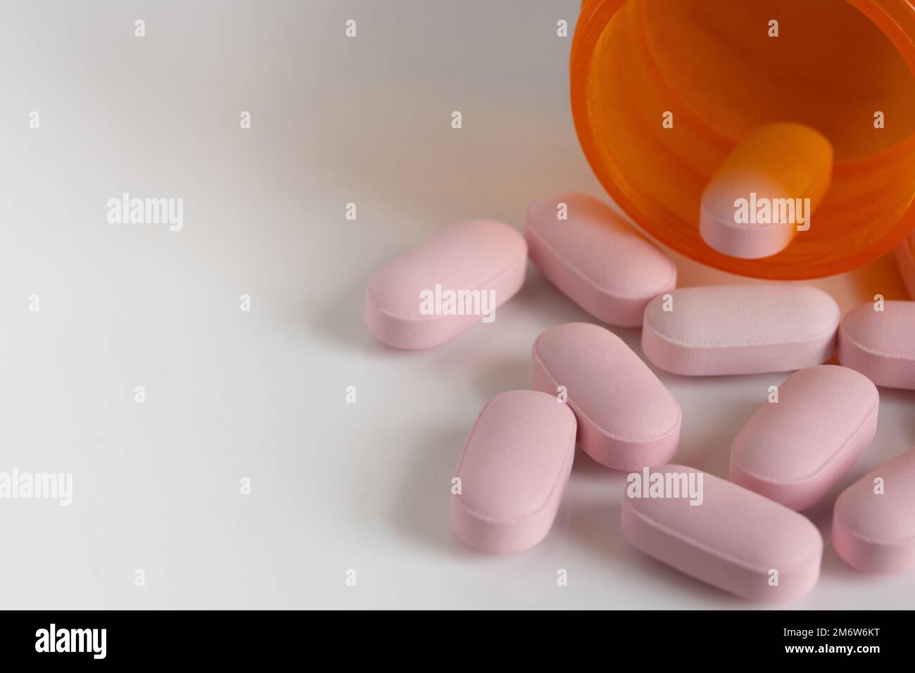 oblong, pink tablet pills spilt from a medicine bottle on a white background with copy space and shallow depth of field Stock Photo