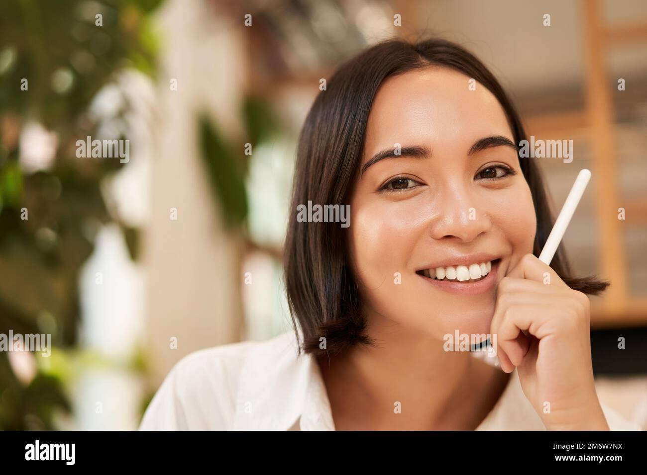 Close up portrait of stylish young brunette woman, sitting with graphic pen and smiling, relaxing in cafe, writing something, ma Stock Photo