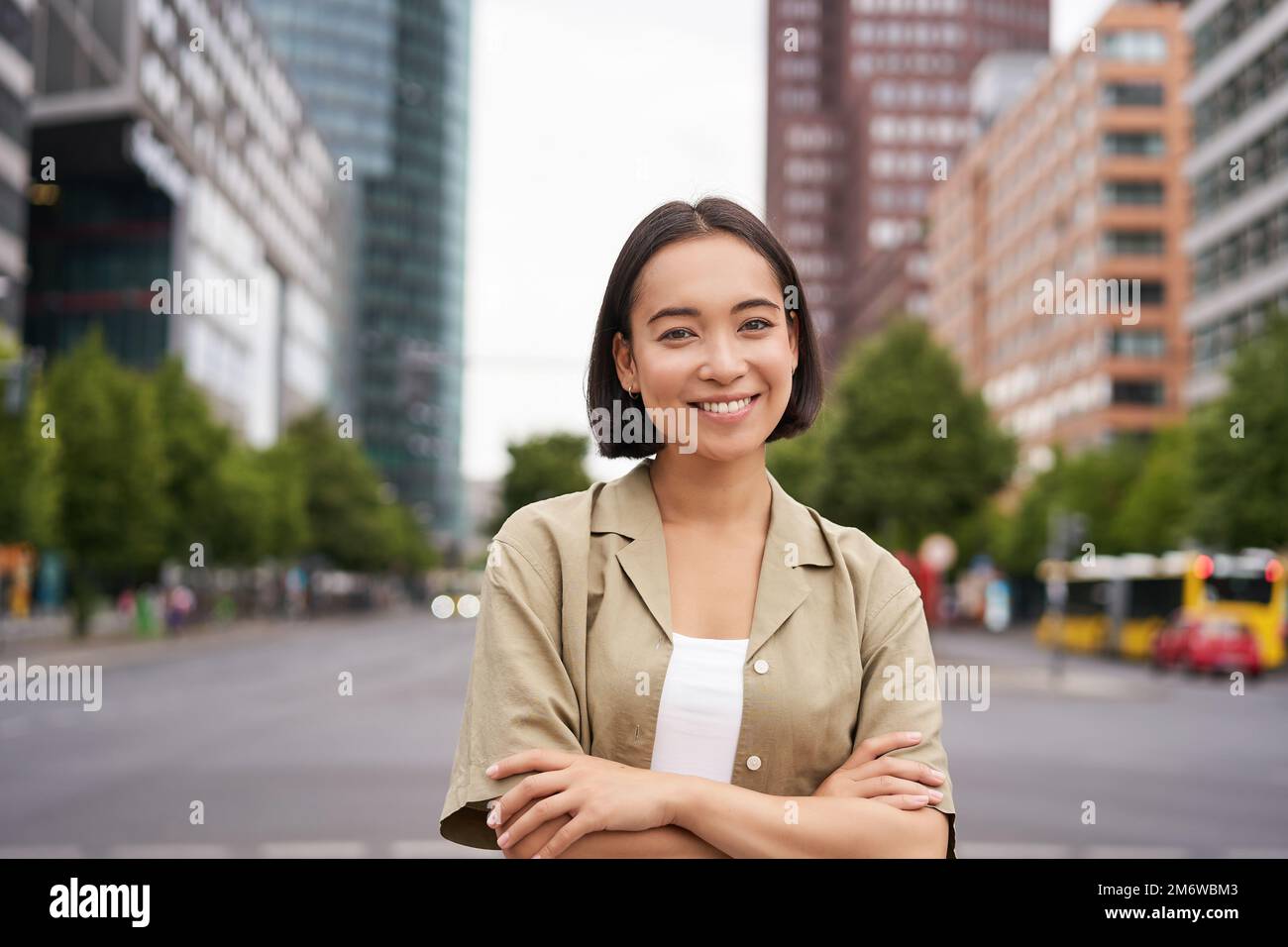 Urban people. Young happy asian girl cross arms on chest, posing on busy city street, smiling with confidence at camera Stock Photo