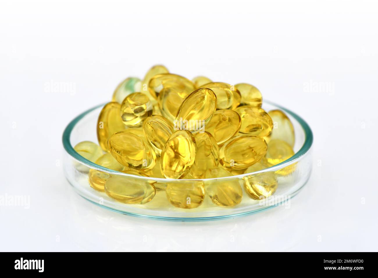Soft gelatin capsules of essential oil in the glass dish isolated on white background. Sample of oil capsules for advertising. Stock Photo
