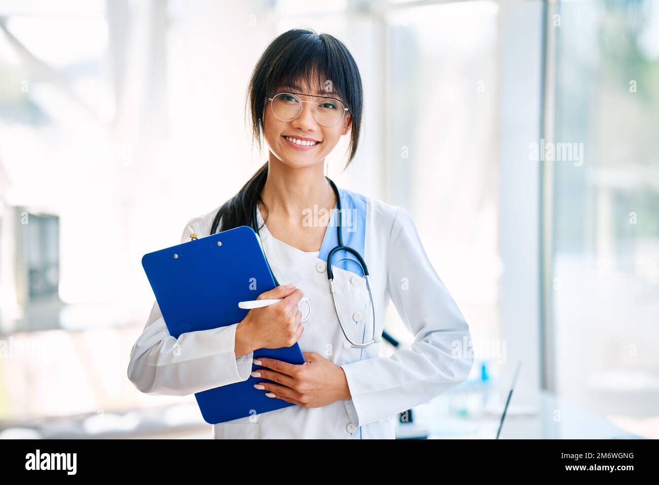 Smiling confident female doctor holding clipboard posing in hospital Stock Photo