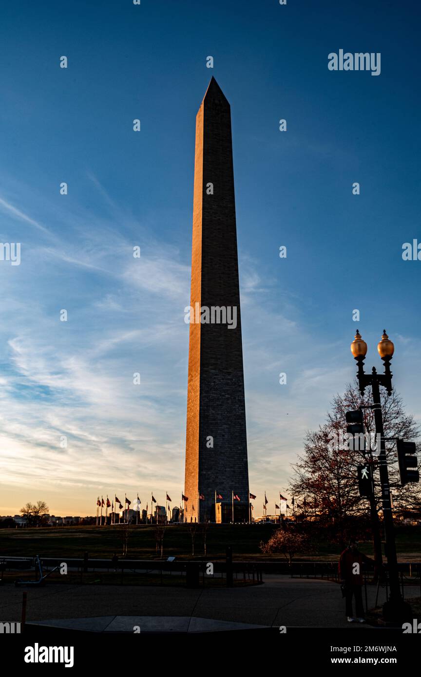 The Washington Monument is a 555-foot tall obelisk located in Washington, D.C. Picture of backlit of obelisk in sunset with few clouds. Stock Photo