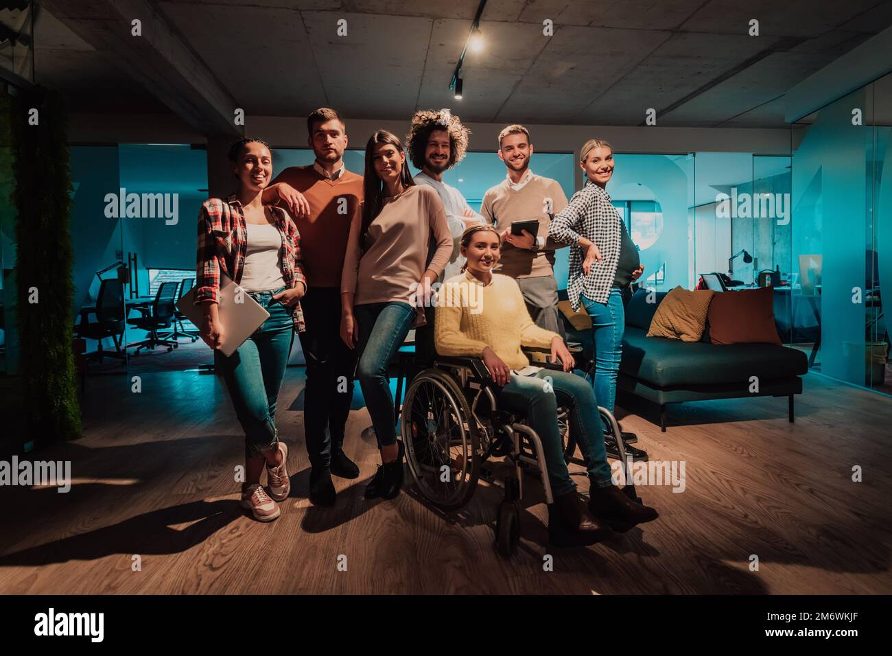 Businesswoman in a wheelchair on break in a modern office with her team in the background Stock Photo