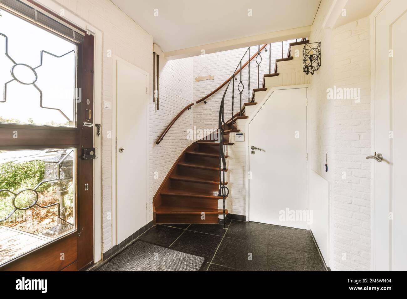 https://c8.alamy.com/comp/2M6WN04/a-staircase-leading-up-to-the-second-floor-in-a-modern-home-with-white-brick-walls-and-black-tiles-on-the-floor-2M6WN04.jpg