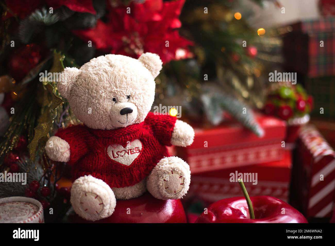 White Teddy bear in red knitted sweater with heart on the chest and the words Love near Christmas tree among the gift boxes. Gif Stock Photo