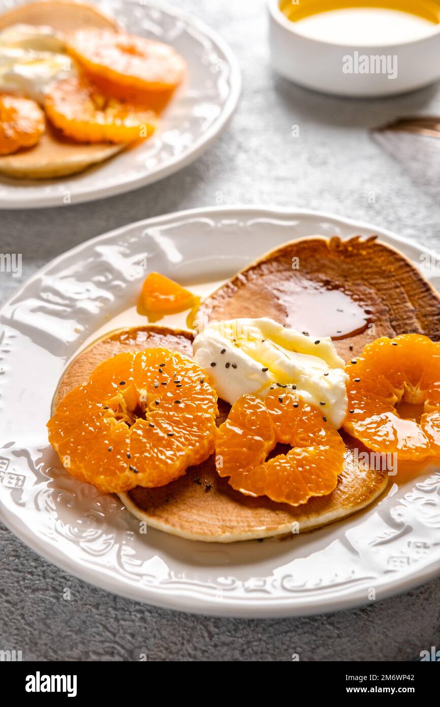 Close-up delicious pancakes with tangerines and honey or maple syrup for breakfast on a light background. Stock Photo