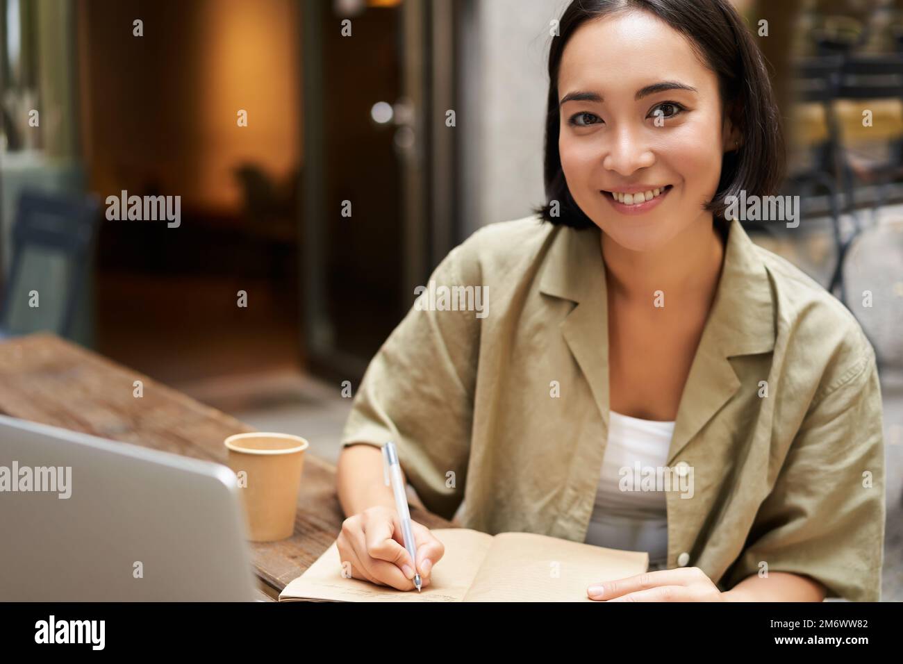 Portrait of young asian woman working on laptop, making notes, writing down while attending online lesson, work meeting Stock Photo