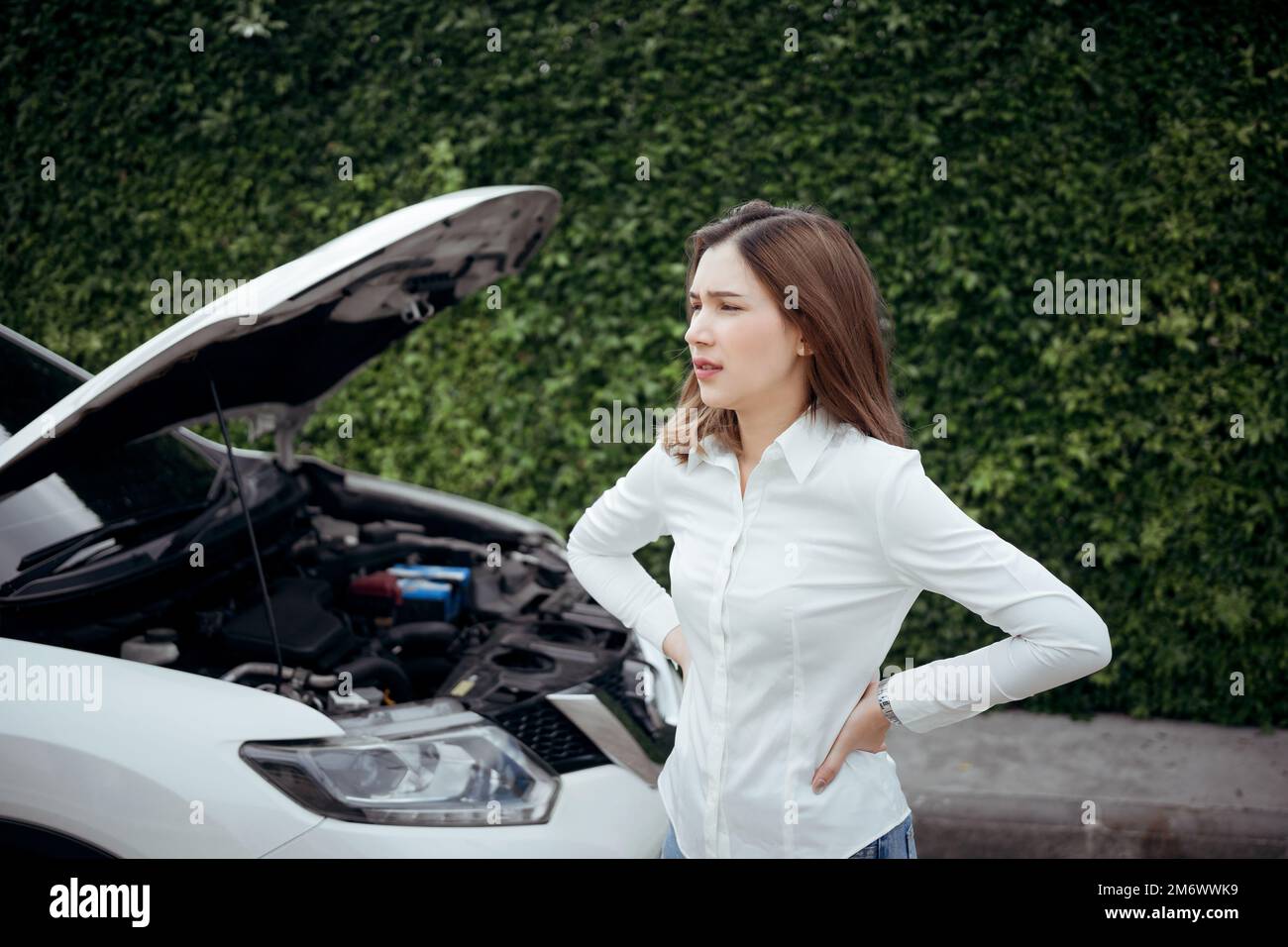 Young woman having car troubles - broken down car on the side of the road, calling the insurance company for assistance. Stock Photo