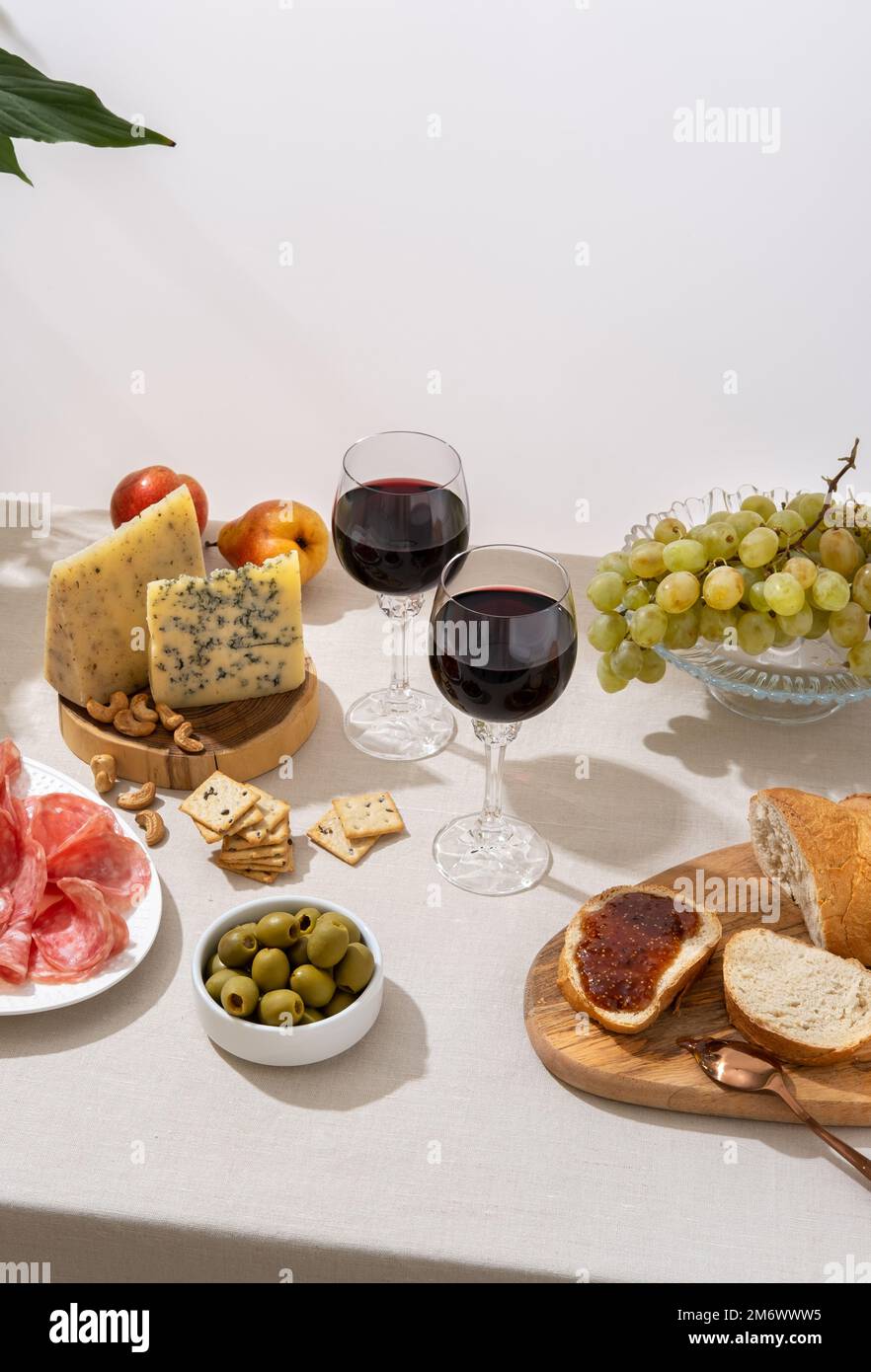 Glasses of red wine with grapes, cheese and salami on light table ...