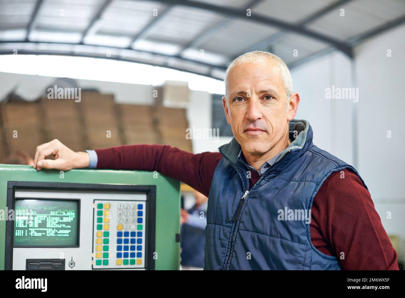 It runs as well as the day it was made. Portrait of a mature man standing next to machinery in a factory. Stock Photo