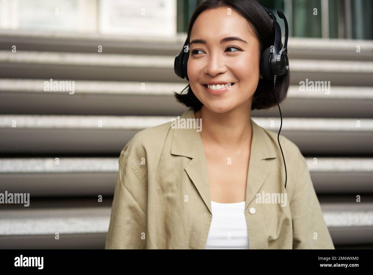Portrait of beautiful girl in earphones, listening music, smiling and walking in city centre Stock Photo