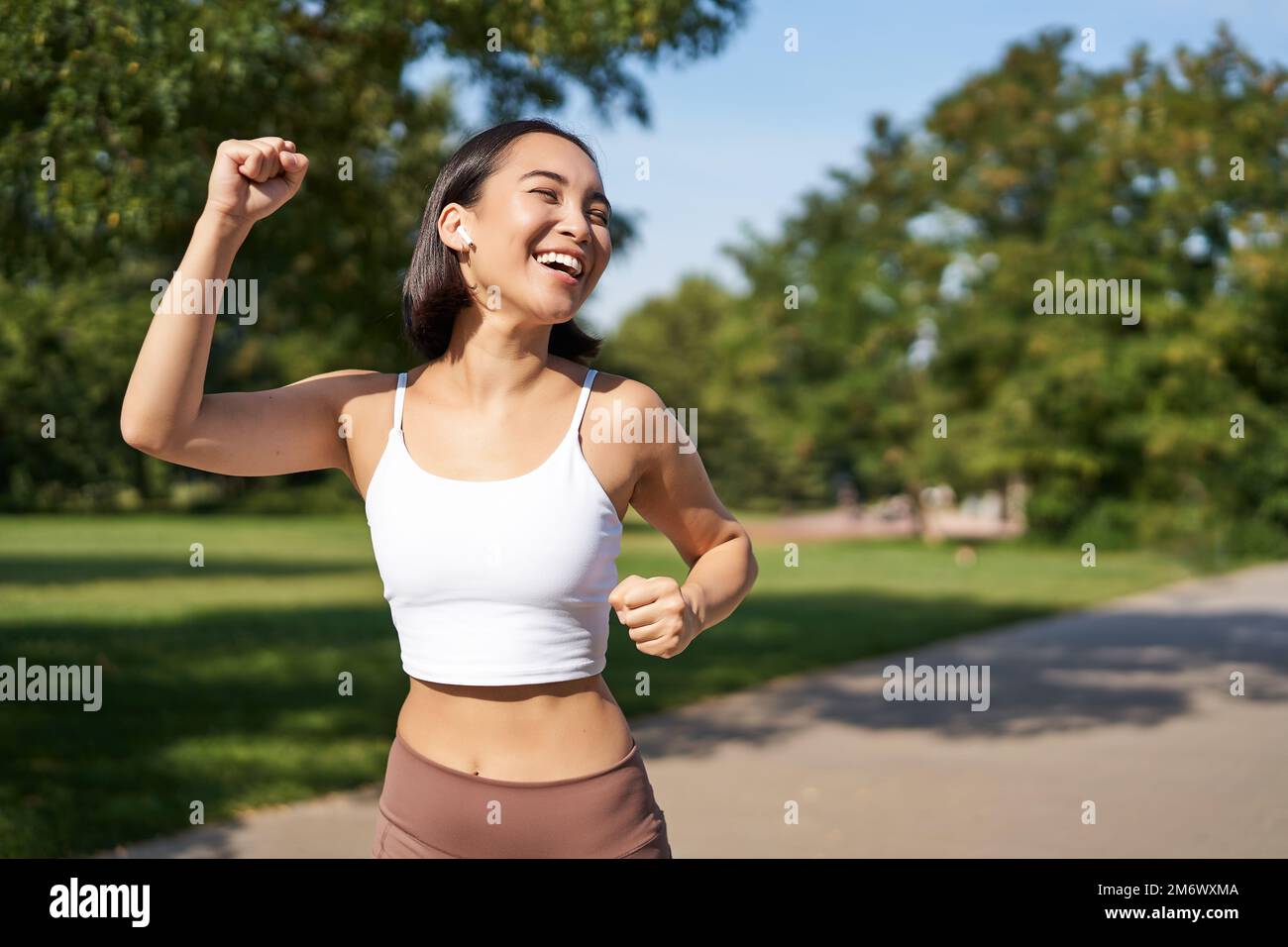 Happy fitness girl achieve goal, finish marathon, running with hands up, celebrating victory while jogging, triumphing in park Stock Photo