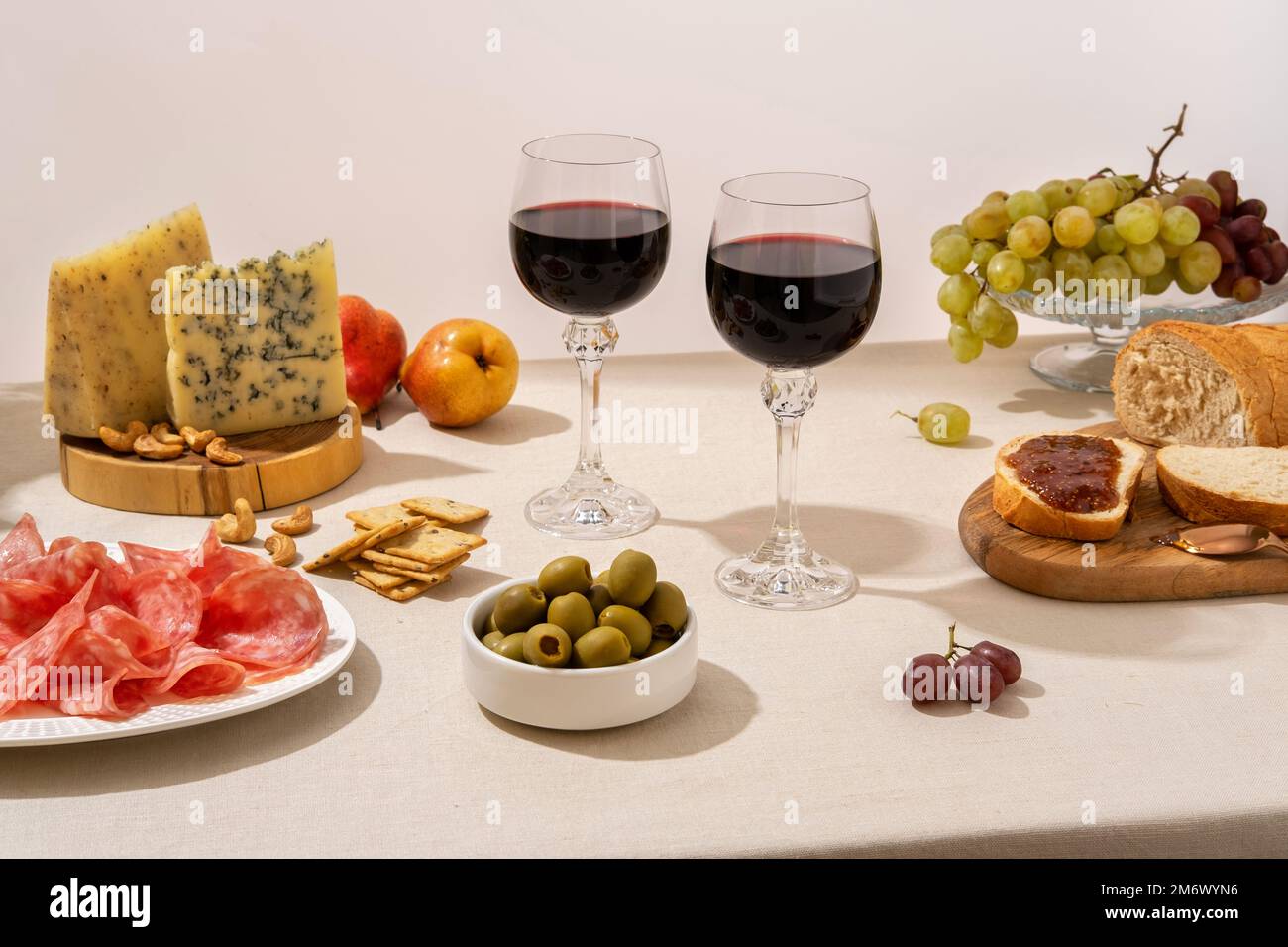 Glasses of red wine with grapes, cheese and salami on light table ...