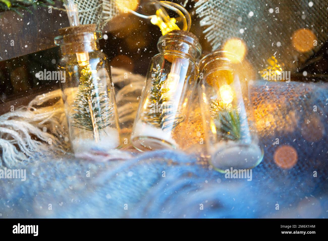 Fairy lights in a jar with a Christmas tree and snow closeup on a warm