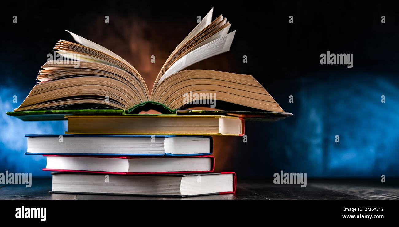 A composition with an open book lying on a stack of other books Stock Photo