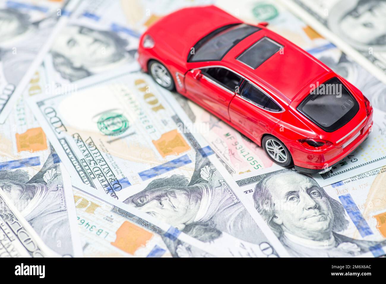 Red toy car is standing on dollar banknotes. Cost of buying a car, fuel